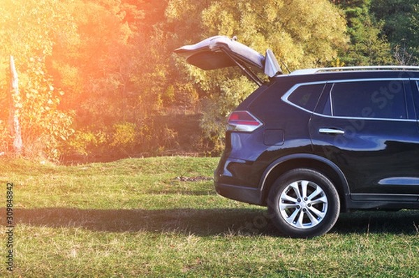 Fototapeta Crossover car with opened boot in a park with trees and sunlight