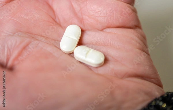 Obraz Nahaufnahme: Zwei weiße Tabletten in der Hand einer Frau - selektiver Fokus auf eine Tablette
