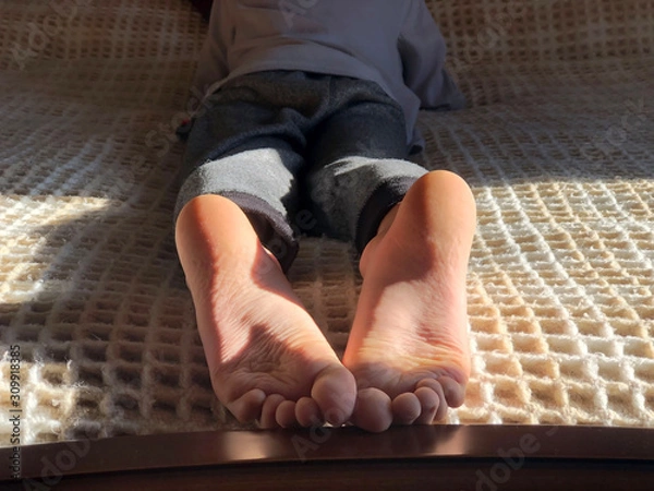 Fototapeta Boy's feet on bed close-up. Boy lying on bed and reading a book