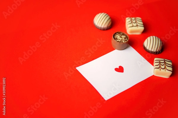 Fototapeta St. Valentine's Day. Chocolate candies and a note with a heart on red background. Chocolate candies. Chocolate treats. Assorted chocolates.