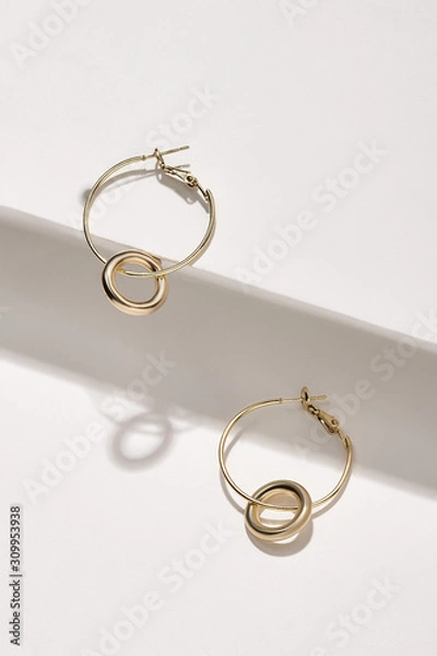 Fototapeta Subject shot of a pair of hoop earrings isolated on the white geometric design surface. Each metal earring is made as a golden ring with a pendant in the form of a thick silver ring.