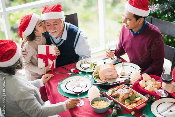 Obraz Big Asian family celebration in Christmas day, daughter hold gift box on hand and kiss grandfather and which smiling and felling happy at home after breakfast time. Merry Xmas and happy new year.