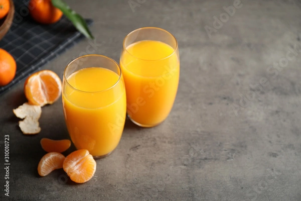 Fototapeta Fresh tangerines and glasses of juice on grey table. Space for text
