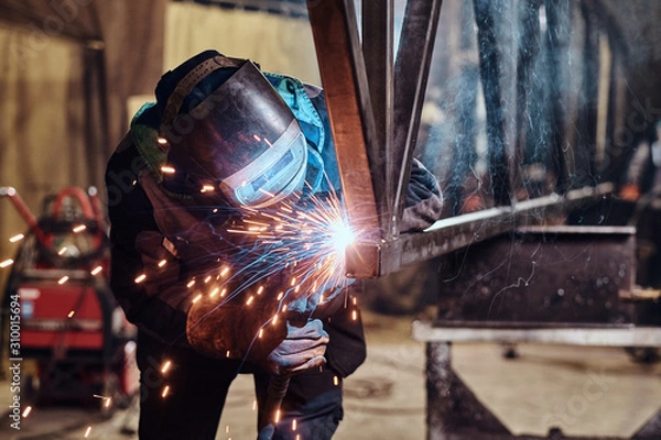 Fototapeta Man is working at metal factory, he is welding a piece of rail using special tools.