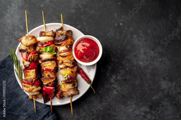 Fototapeta Meat skewers with grilled vegetables on a white plate on a stone background with copy space for your text