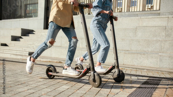 Obraz Lets ride. Girl and boy having fun driving electric scooters on a sunny day