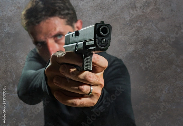 Fototapeta shallow depth of focus action portrait of serious and attractive hitman or special agent man holding gun pointing the weapon isolated on dark background