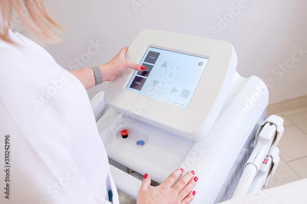 Fototapeta Rear view of a female beautician in white coat presses on display of device to select desired procedure. Concept of modern high-tech equipment for anti-aging procedures. medical examination of patient