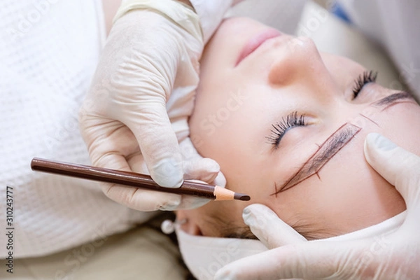 Obraz Close-up of the hand of a beauty master woman sketching a new eyebrow shape to a young female client. Concept of eyebrow tattoo and microblading