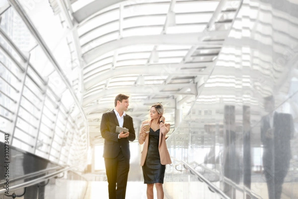 Fototapeta Businessman and businesswoman discussing while walking outside office in modern city. Business colleague discussing about their job on the way, man holding digital tablet and woman drinking morning co