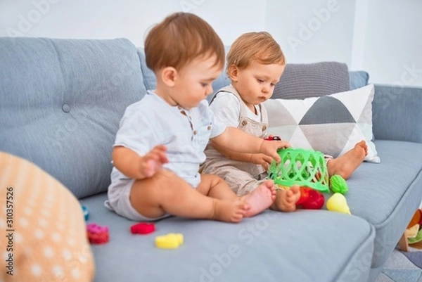 Fototapeta Beautiful toddlers sitting on the sofa playing with toys at home