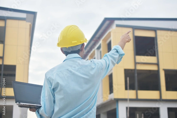 Obraz Engineering holding computer notebook with yellow hard hat working building construction estate