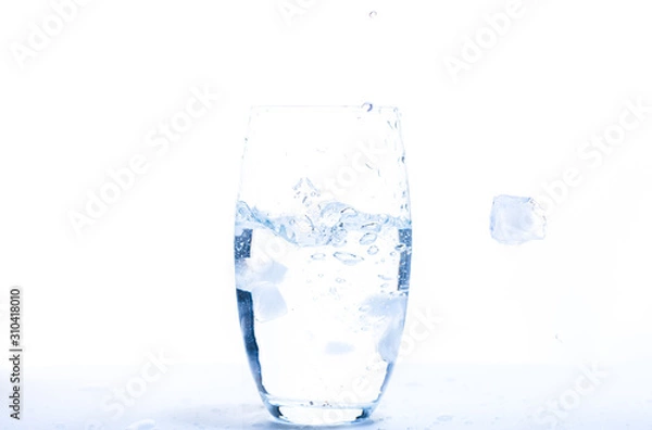 Fototapeta falling ice cube into a water glass making bubbles with a with background 