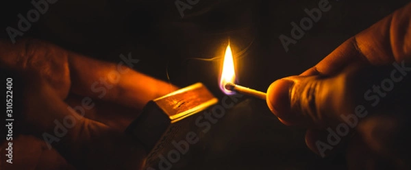 Obraz A match lit in the dark in hands with a matchbox