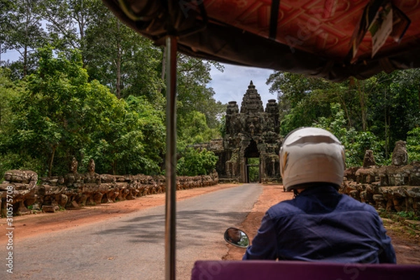 Fototapeta View from the Tuk Tuk (Rickshaw) on the gate to the Angkor Thom ancient temple in Siem Reap, Cambodia. Tourists take the tour around the old temples for the whole day and traveling with the driver.