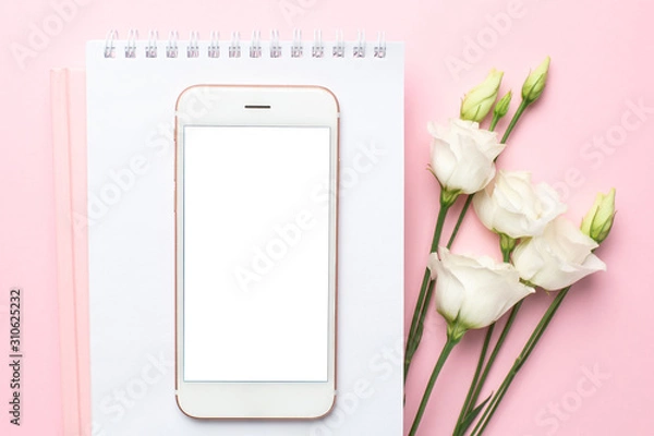 Fototapeta Mobile phone, white eustoma flower and notebook on pink background.Women's business technology composition