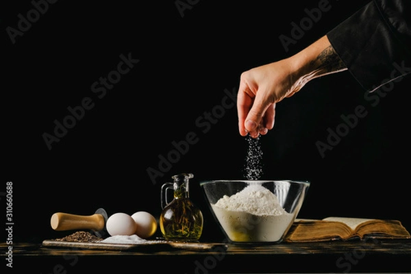 Fototapeta Dough preparation process. Chef adds ingredients to flour on a black background.