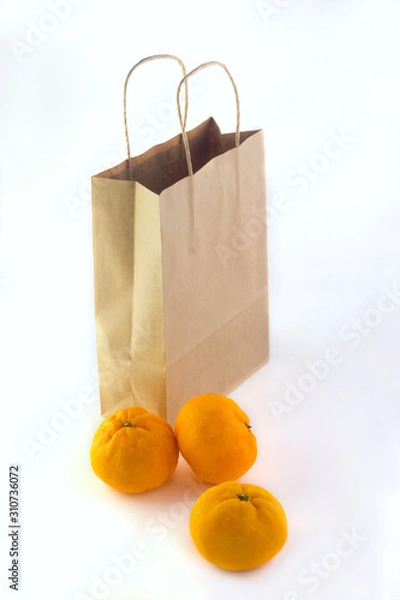 Fototapeta  tangerines lying near a paper craft package on a white background