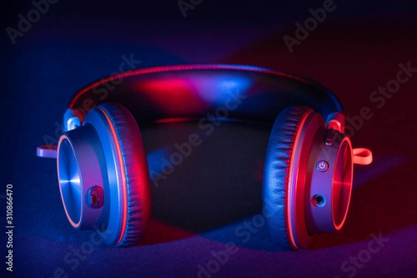 Obraz A pair of generic headphones made of brushed metal with a leather headband lit with a red and blue flash gels