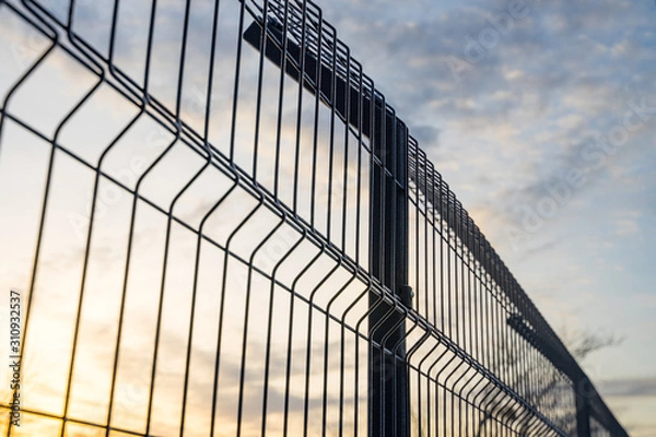 Fototapeta Steel grating fence made with wire on blue sky background. Sectional fencing installation