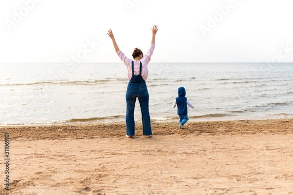 Fototapeta Woman with a child on the beach in front of open water. The child runs away.