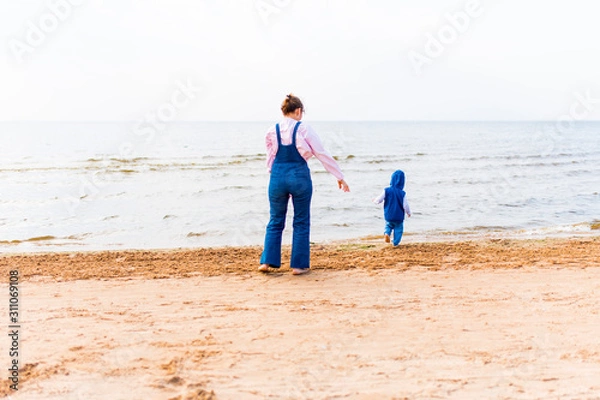 Fototapeta The child runs away into the sea. Woman with a child on the beach in front of open water.