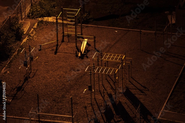 Fototapeta Aerial shot of an empty sport field at night in a dark yard with long shadows. One street lamp