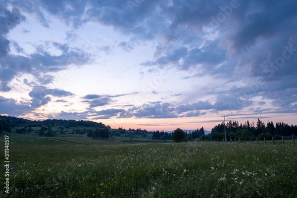 Fototapeta The colors of the sky after sunset with clouds above the mountain meadow.