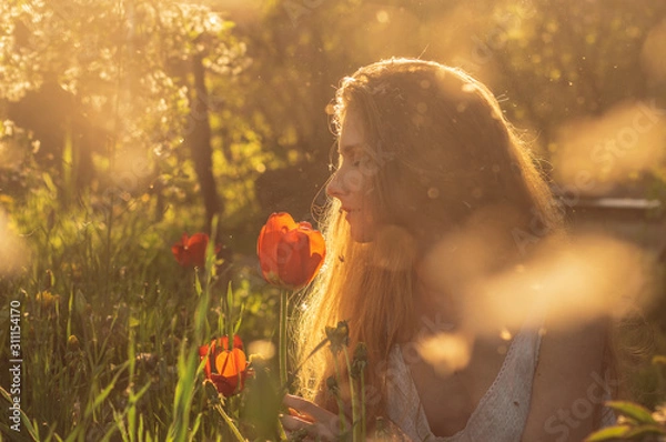 Obraz Girl in white dress smelling tulip in sunset among fluff, dandelions and cherry flowers