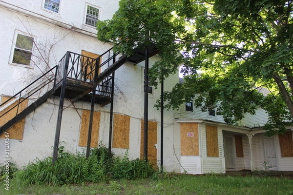 Fototapeta Old abandoned weathered boarded up historic country farmhouse with boarded up windows and peeling paint