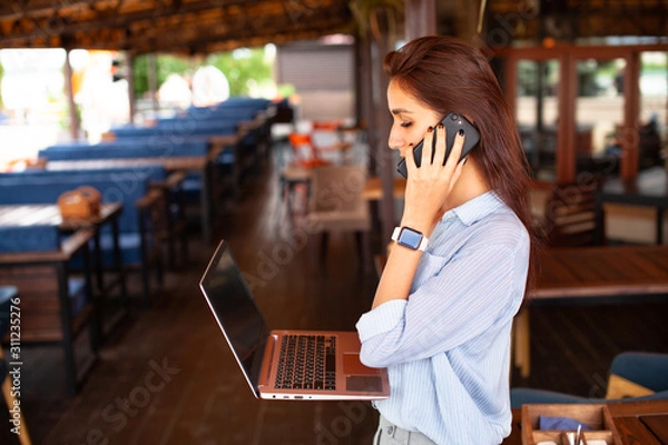 Fototapeta Portrait of female restaurant manager. Businesswoman work with laptop and mobile phone in cafe.