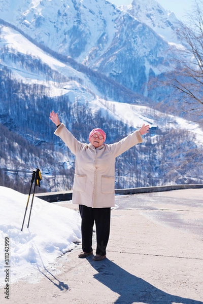 Obraz Portrait of a happy elderly woman in nature. Cute old woman smiles and does Nordic walking in the spring on a Sunny day. The way of life of the elderly the concept of retirement.