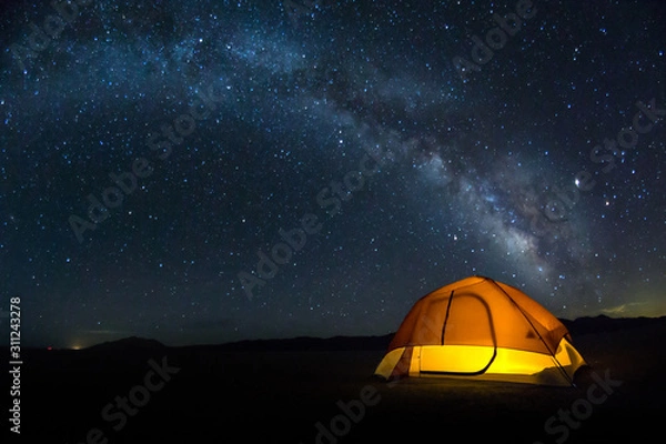 Fototapeta Lit tent on the playa under a bright Milky Way arch of stars