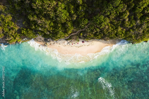 Obraz View from above, stunning aerial view of some tourists sunbathing on a beautiful beach bathed by a turquoise rough sea during sunset, Green Bowl Beach, South Bali, Indonesia.