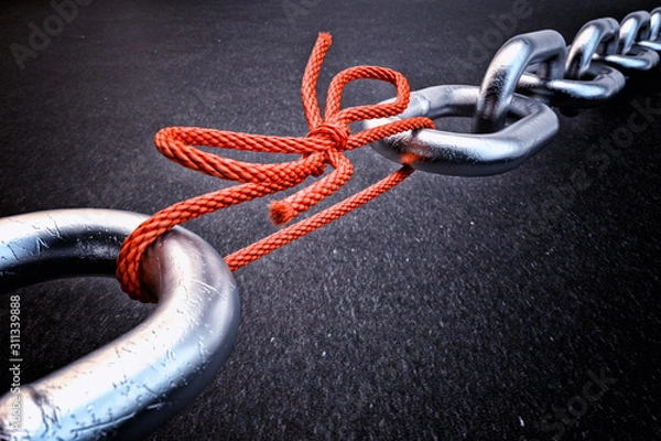 Fototapeta Weakest link, security break fix and strength concept, metallic chain connected by a red knotted rope on black background
