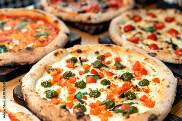 Fototapeta A lot of different freshly prepared pizza on a wooden table in an Italian restaurant