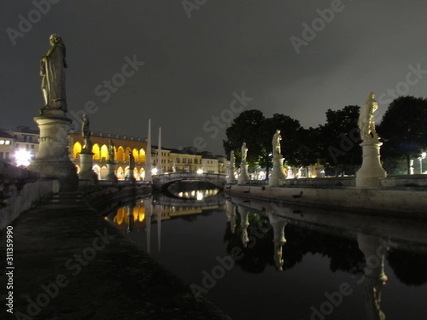 Fototapeta Padova, Italy - October 12th, 2019: Prato della Valle, in Padova, at night. The biggest square in Italy and one of the biggest in Europe, surrounded by a canal of water and by two rings of statues.