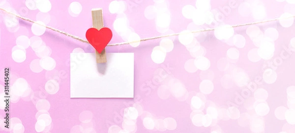 Fototapeta Happy Valentine's Day background banner - White paper note hang on wooden clothes pegs with wooden hearts on a string isolated on pink texture and bokeh lights, with space for text