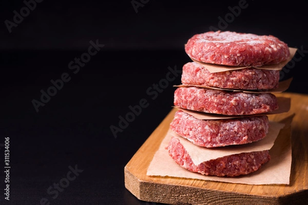 Obraz frozen raw minced meat in the form of cutlets on a black background. have copy space