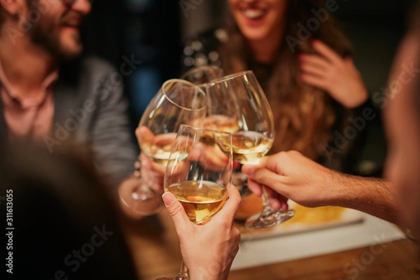 Fototapeta Best friends sitting in restaurant for dinner and making a toast with white wine. On table is food.