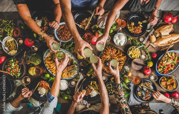 Fototapeta Flat-lay of family clinking glasses over table with Turkish cuisine lamb chops, quince, bean, vegetable salad, babaganush, rice pilav, pumpkin dessert and lemonade, top view. Middle East cuisine