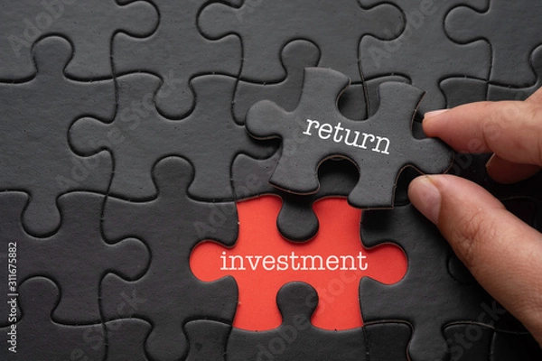 Fototapeta Hand hold piece of puzzle written RETURN revealing word INVESTMENT. Business concept.