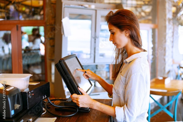 Fototapeta Close-up view of waitress registrated orders to the payment terminal. Young and beautiful waitress stand near sale terminal and check the order.
