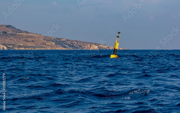 Fototapeta Yellow and black steel navigational floating buoy - West cardinal mark - in the blue Mediterranean sea water between Comino and Malta islands.
