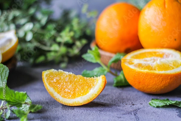 Fototapeta Photo of fresh orange on retro background. A slice of orange with green leaves. Half of orange on wooden plate bowl. Free space for text. Dark background. Image