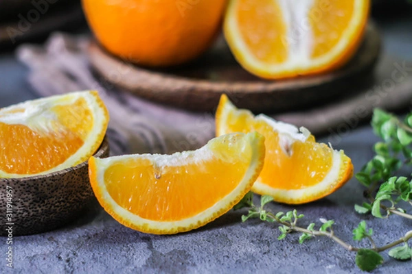 Fototapeta Photo of fresh orange on retro background. A slice of orange with green leaves. Half of orange on wooden plate bowl. Free space for text. Dark background. Image