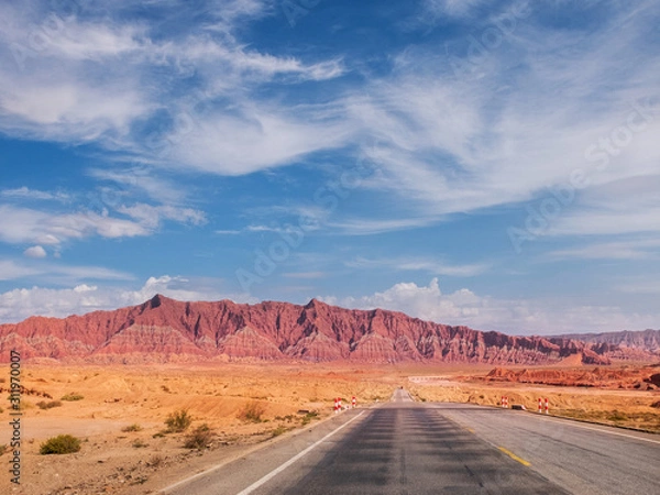 Fototapeta The red rock formations of Danxia landform with empty highway in Xinjiang of China
