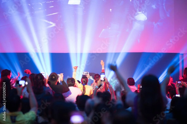 Obraz Rear view of crowd with arms outstretched at concert or seminar training in hall