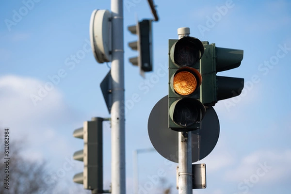 Fototapeta Germany, Berlin yellow traffic light, blue sky, clouds and tree in background 