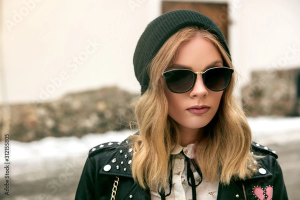 Obraz portrait of an urban girl in a leather jacket wearing sunglasses and a black hat during a snowywinter